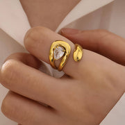 Gold ring with a clear gemstone on a hand against a neutral background